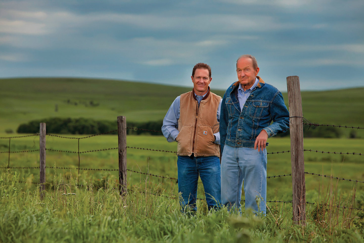 Two men standing in a field with a barbed wire fence behind them.